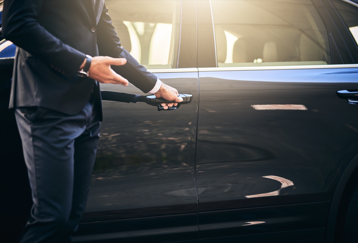 Business woman beside a luxury car as a driver opens the vehicle door